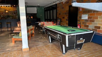 A billiards table in a room with a brick floor, a bar area with stools, and a chandelier.