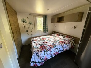 A bedroom with a bed, a window with curtains, a wall-mounted shelf, and a door.