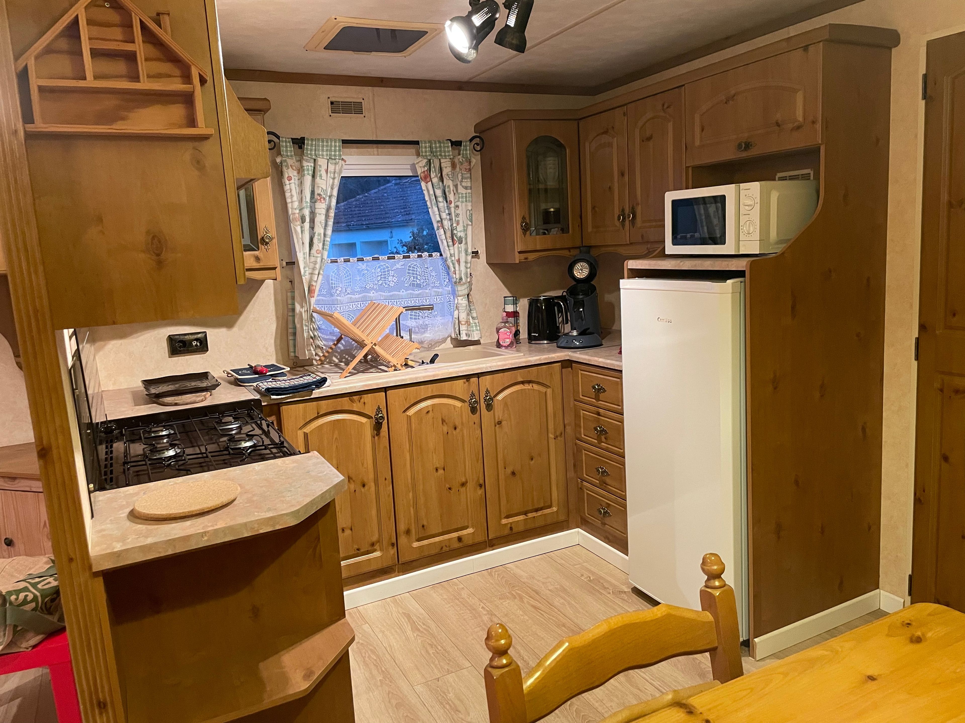 Una cocina compacta con armarios de madera, microondas, estufa y una ventana con cortinas.