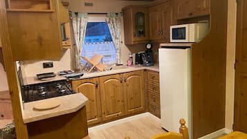 Una cocina compacta con armarios de madera, microondas, estufa y una ventana con cortinas.
