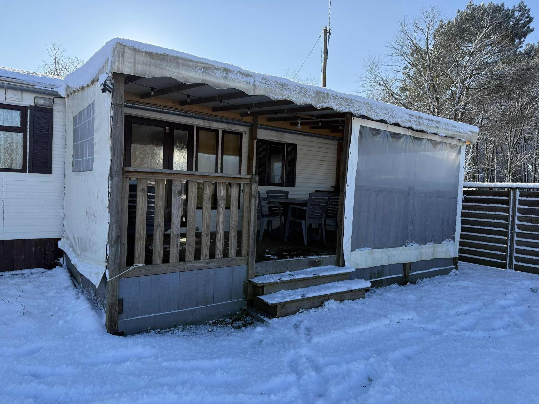 Une petite maison mobile d’un seul étage, dotée d’un porche et d’un espace extérieur aménagé et abrité.