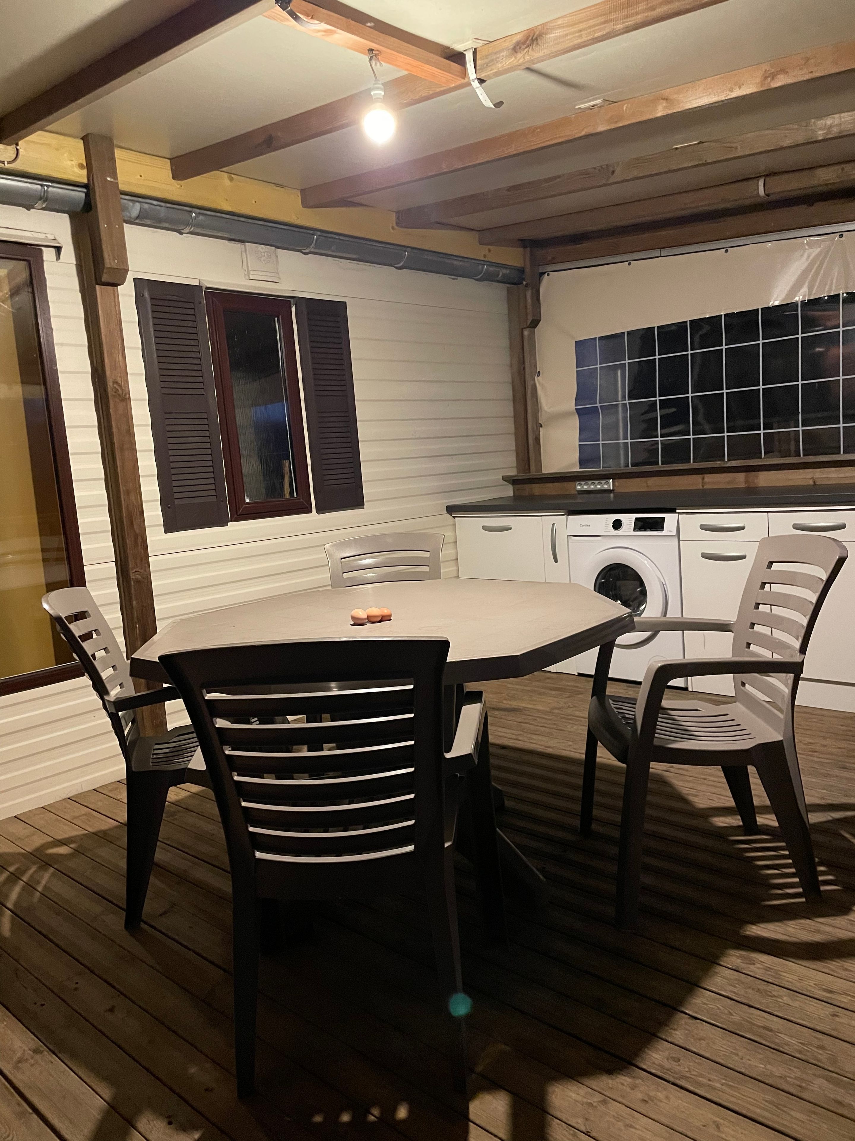 Un coin repas avec une table et des chaises, un lave-linge et une fenêtre avec des volets.