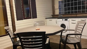 Un coin repas avec une table et des chaises, un lave-linge et une fenêtre avec des volets.