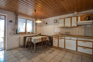A kitchen with wooden cabinets, a dining table with chairs, a window with curtains, and a clock on the wall. - Apartment 'Im Bauernhaus' with Mountain View, Shared Terrace and Shared Garden (Oberharmersbach)