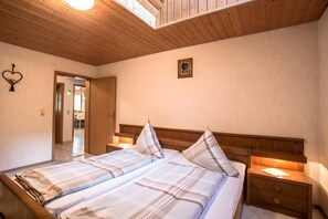 Une chambre d’hôtel avec un plafond en bois, un lit recouvert d’une couette à carreaux, une table de chevet et un tableau accroché au mur.