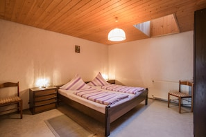 A bedroom with a wooden ceiling, a bed with striped bedding, a nightstand, a chair, and a radiator. - Apartment 'Im Bauernhaus' with Mountain View, Shared Terrace and Shared Garden (Oberharmersbach)