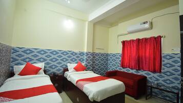 Habitación de hotel con dos camas, un sofá rojo, una mesita y un equipo de aire acondicionado.