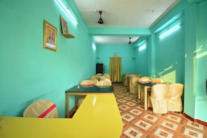 A room with teal walls, a patterned floor, and a yellow table. There are chairs with headrests and a ceiling fan. - Hotel O Gloria Inn (Agartala)