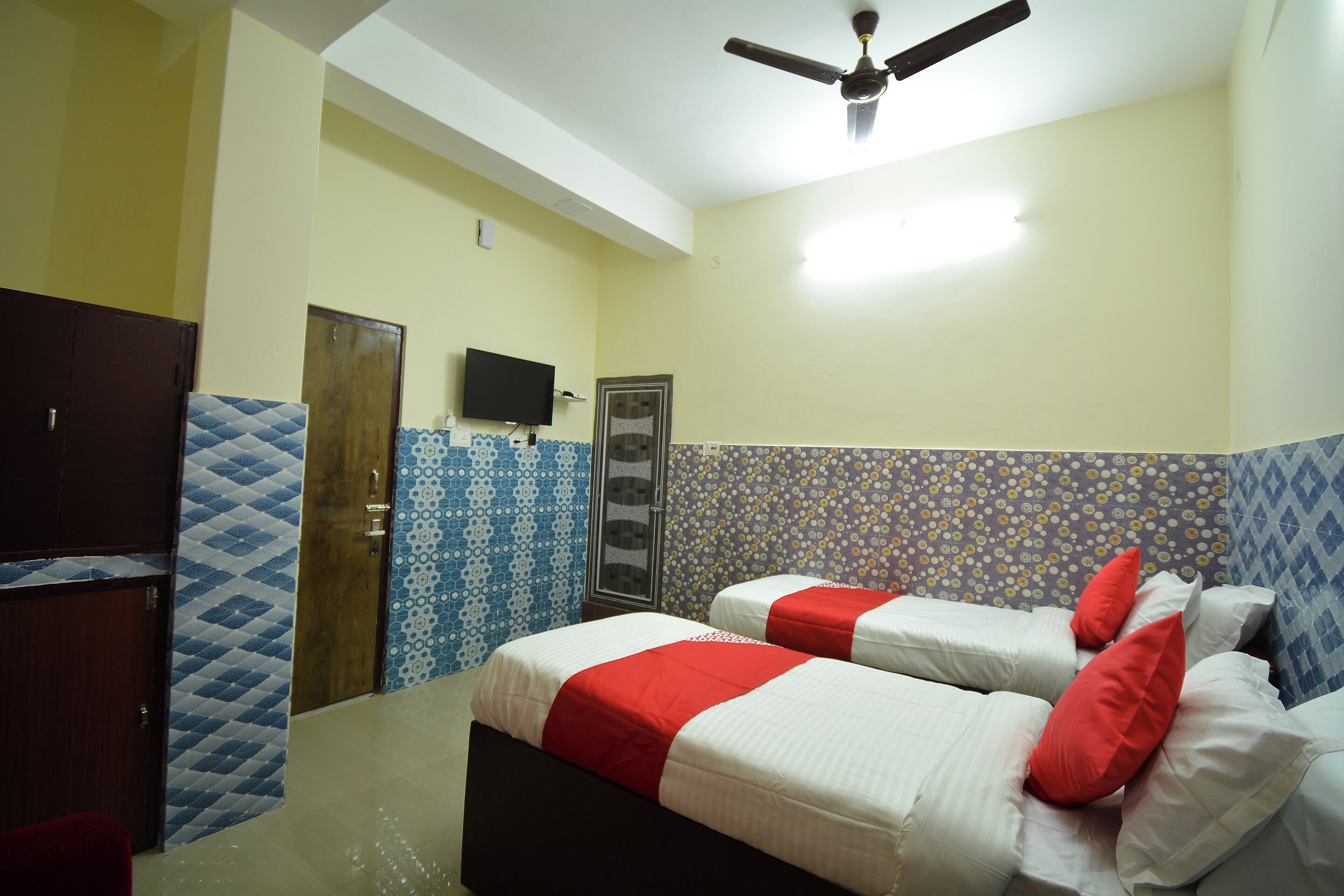 Habitación de hotel con dos camas, ventilador de techo, televisión y paredes con diseño.