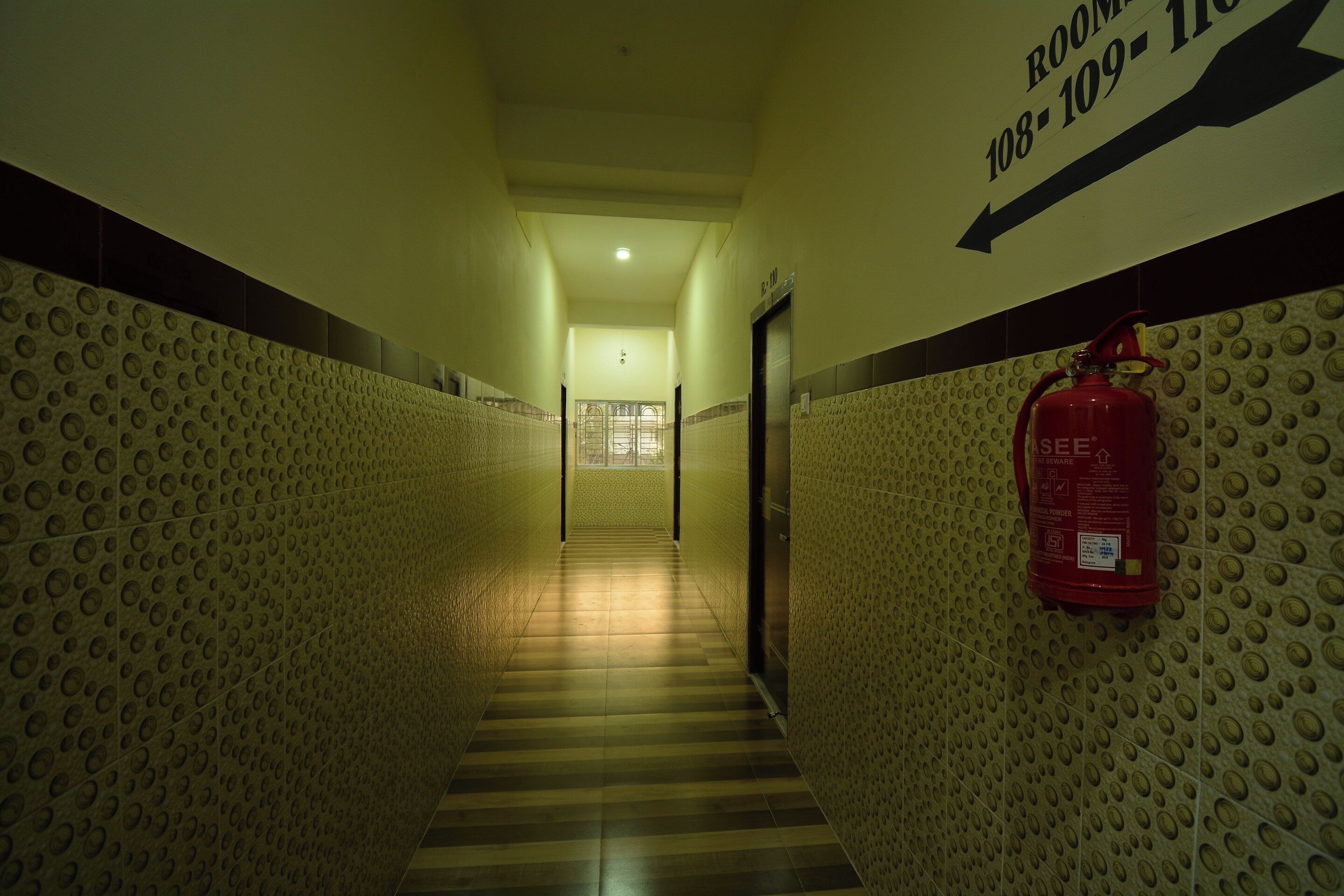 A hallway with a fire extinguisher mounted on the wall, a directional sign, and a tiled floor.