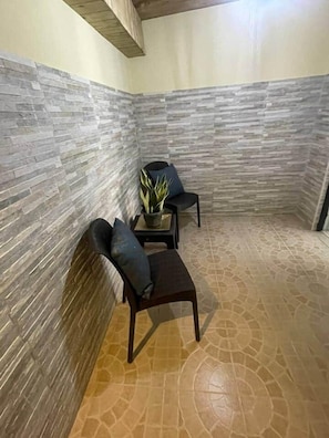 Ein Eckzimmer mit Steinwänden, einem gemusterten Boden, einem dunklen Holztisch, einem Stuhl und einem Blumentopf.