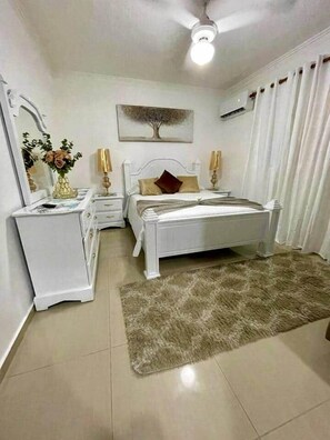 A bedroom with a bed, bedside tables, a dresser, a mirror, a ceiling fan, and a rug. - Jacuzzi Privado/ Patio Climatizado / TV 75” / A/C (Santo Domingo Este)