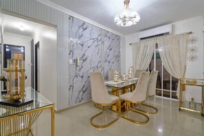 A dining area with a marble wall, a chandelier, and a glass table with gold legs. - Jacuzzi Privado/ Patio Climatizado / TV 75” / A/C (Santo Domingo Este)