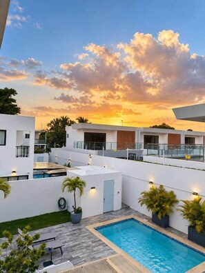 Ein Poolbereich im modernen Stil mit Sonnenuntergangsblick, umgeben von weißen Gebäuden und Palmen.