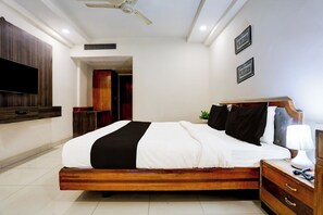 Habitación de hotel con cama, mesita de noche, lámpara y un televisor de pantalla plana montado en la pared.