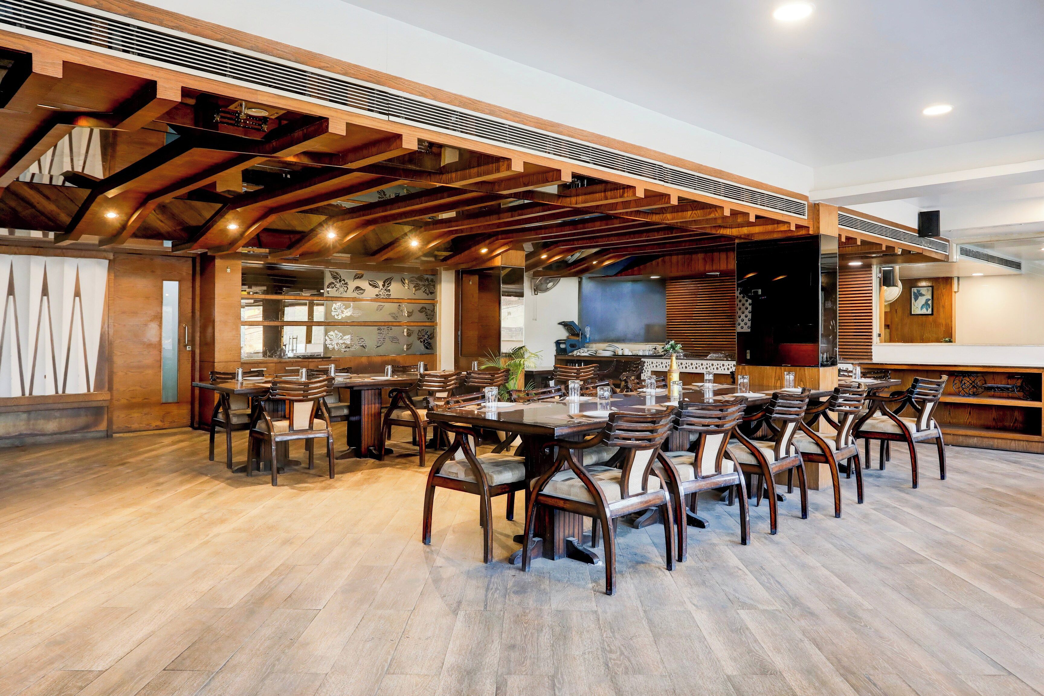 A spacious restaurant with wooden beams and a high ceiling. Tables and chairs are arranged for dining.