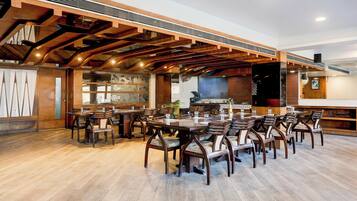 A spacious restaurant with wooden beams and a high ceiling. Tables and chairs are arranged for dining.