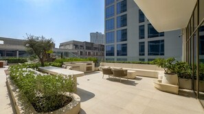 A rooftop terrace with outdoor seating, potted plants, and a view of surrounding buildings. - Peaceful 1BR with Serene Community Views, Just Steps from the Park (Dubai)