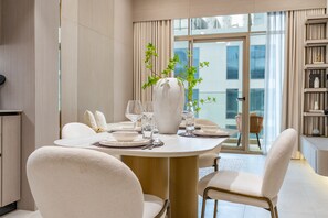 A dining area with a round table set for four, surrounded by white chairs with gold frames. - Peaceful 1BR with Serene Community Views, Just Steps from the Park (Dubai)