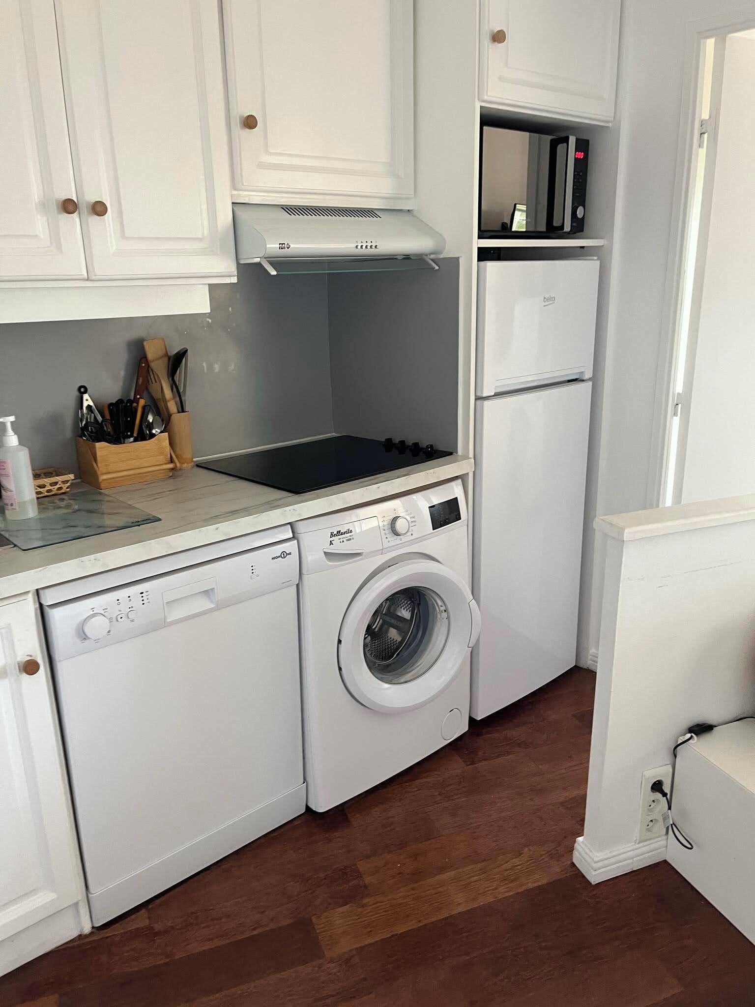 Une cuisine compacte équipée d’un lave-linge, d’un four à micro-ondes et d’un réfrigérateur.