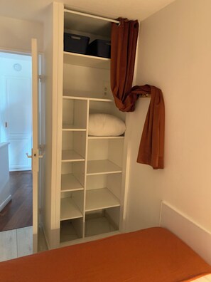 Et værelse med et hvidt skab, et brunt gardin og en seng med et orange sengetæppe.