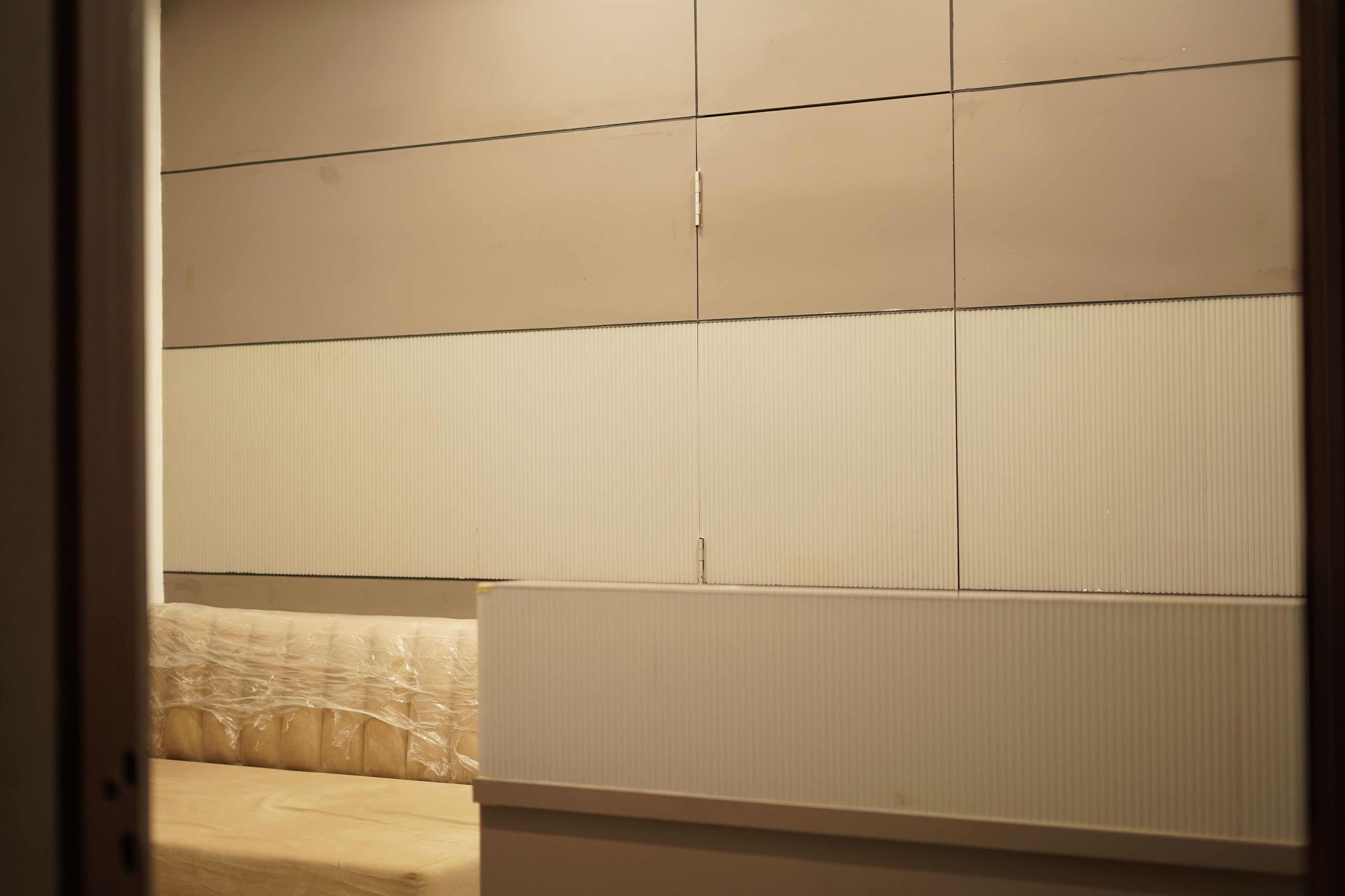 A room with a bed, a window with blinds, and a wall with a textured panel.