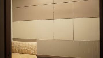 A room with a bed, a window with blinds, and a wall with a textured panel.