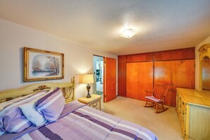 Una camera da letto con un letto, un comodino, una lampada, un armadio in legno, una poltrona a dondolo e un quadro appeso al muro.