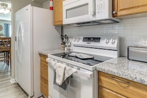 A kitchen with a white refrigerator, stove, and microwave. There are wooden cabinets and a granite countertop. - Tiger Town Retreat: Spacious 2-unit Combo! (Baton Rouge)