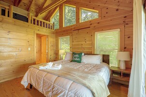 Un dormitorio de cabaña de madera con una cama, dos mesitas de noche y una ventana.