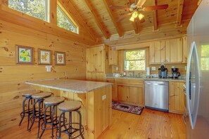 A wooden cabin interior with a kitchen, bar stools, and a refrigerator. - Hot Tub, Fire Pit, Views & More: Blowing Rock Gem (Blowing Rock)