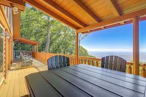 A wooden deck with a table and chairs, overlooking a forested area and distant mountains. - Hot Tub, Fire Pit, Views & More: Blowing Rock Gem (Blowing Rock)