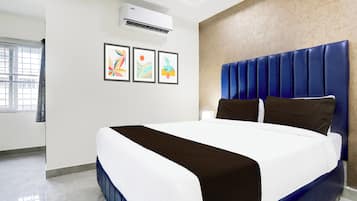 Quarto de hotel com cama grande, ar-condicionado fixado na parede e três obras de arte emolduradas.