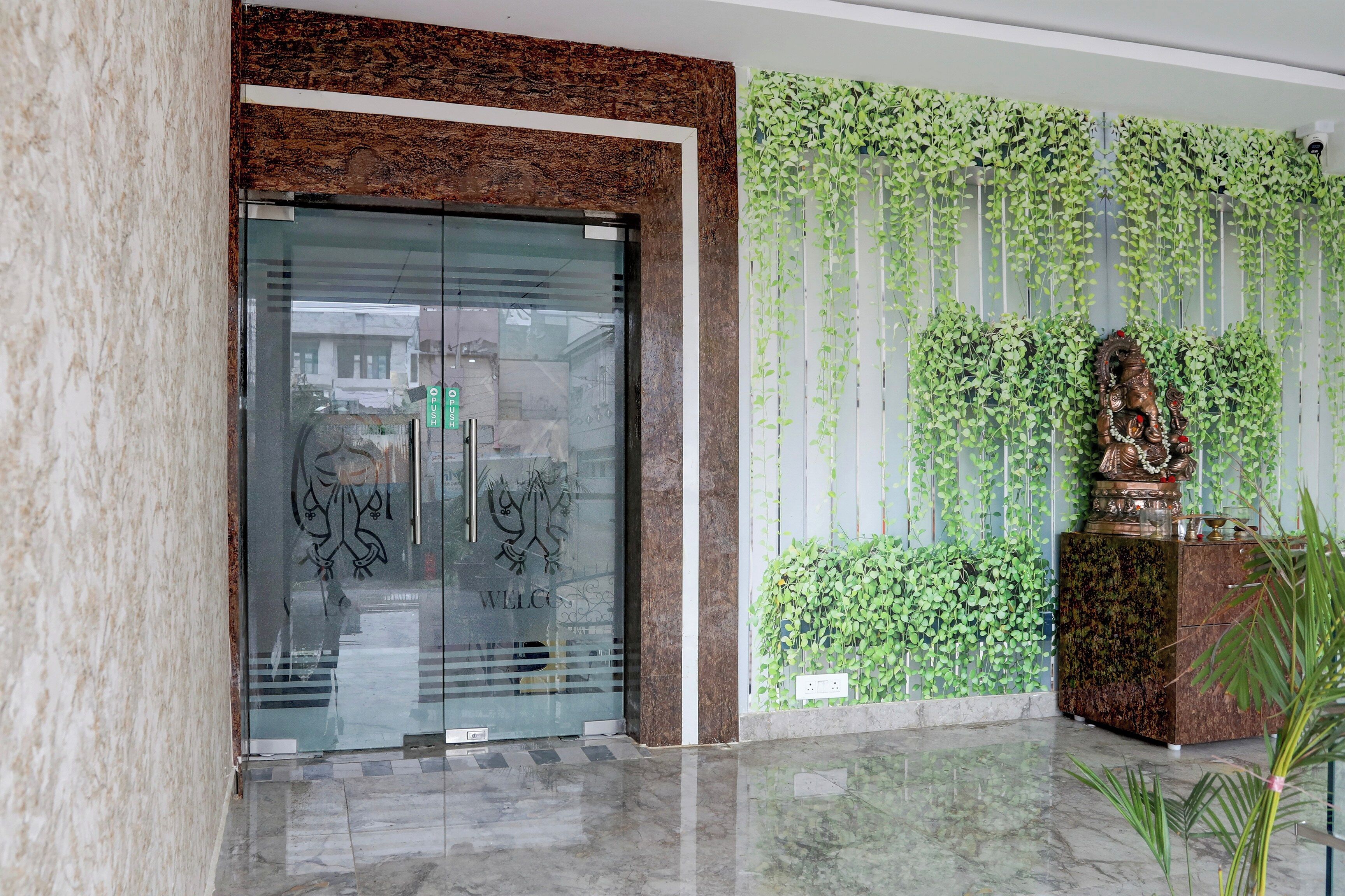 Un área de recepción con puerta de vidrio, una pared con plantas colgantes y una estatua.
