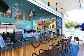 A bar area with a poolside view, including a counter with various items, seating, and a ceiling fan. - Resort Perks! Family Condo 4 Mi to Disney World! (Kissimmee)