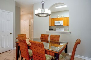 Un coin repas avec une table en verre et des chaises en osier, une cuisine avec des meubles en bois et une porte blanche.