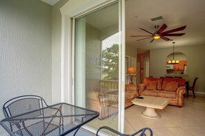 A balcony with a table and chairs, a sliding glass door leading to a living room with a sofa and a ceiling fan. - Resort Perks! Family Condo 4 Mi to Disney World! (Kissimmee)