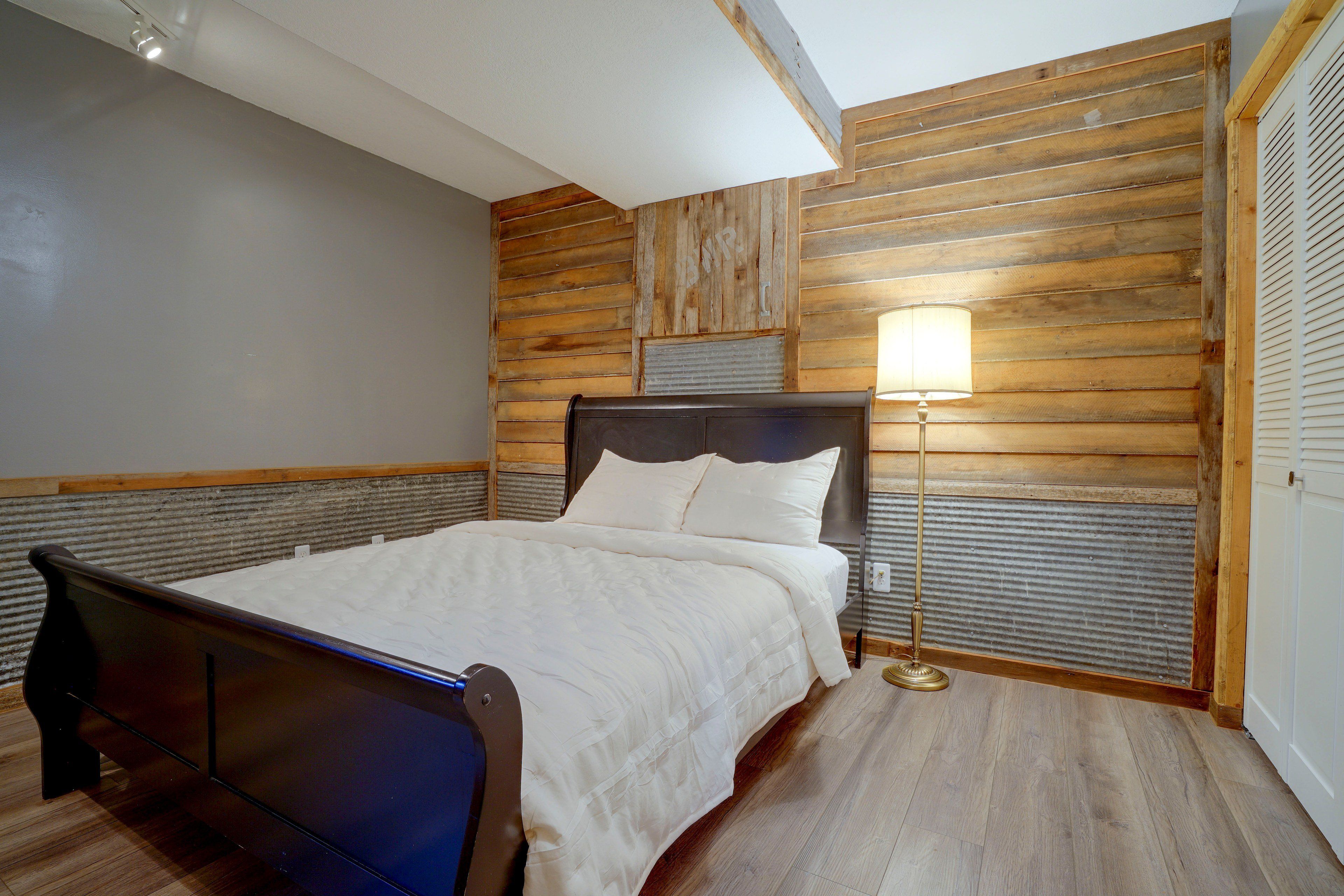 A bedroom with a wooden headboard, a bed with white bedding, a bedside lamp, and a wooden floor.