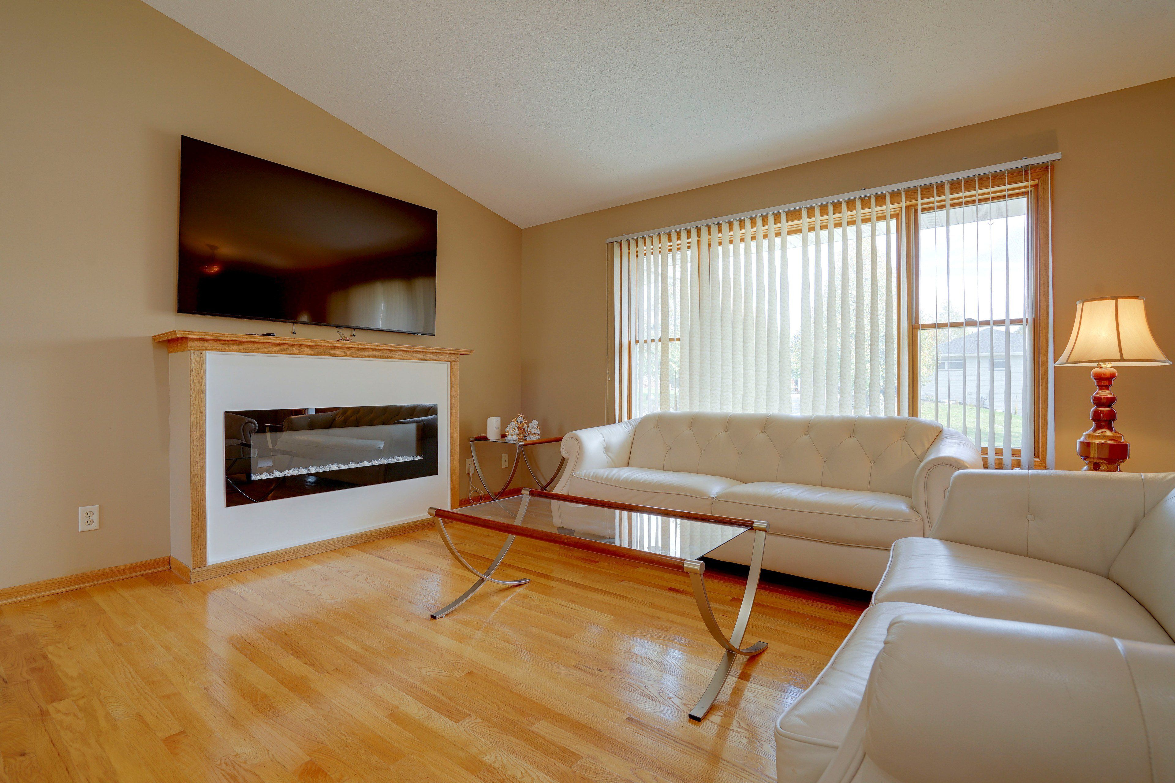 A living room with a flat-screen TV mounted above a fireplace, a white sofa, and a glass coffee table.