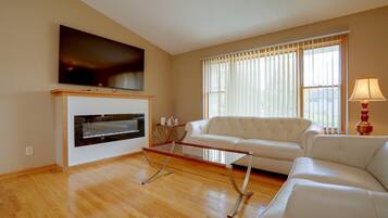 A living room with a flat-screen TV mounted above a fireplace, a white sofa, and a glass coffee table.