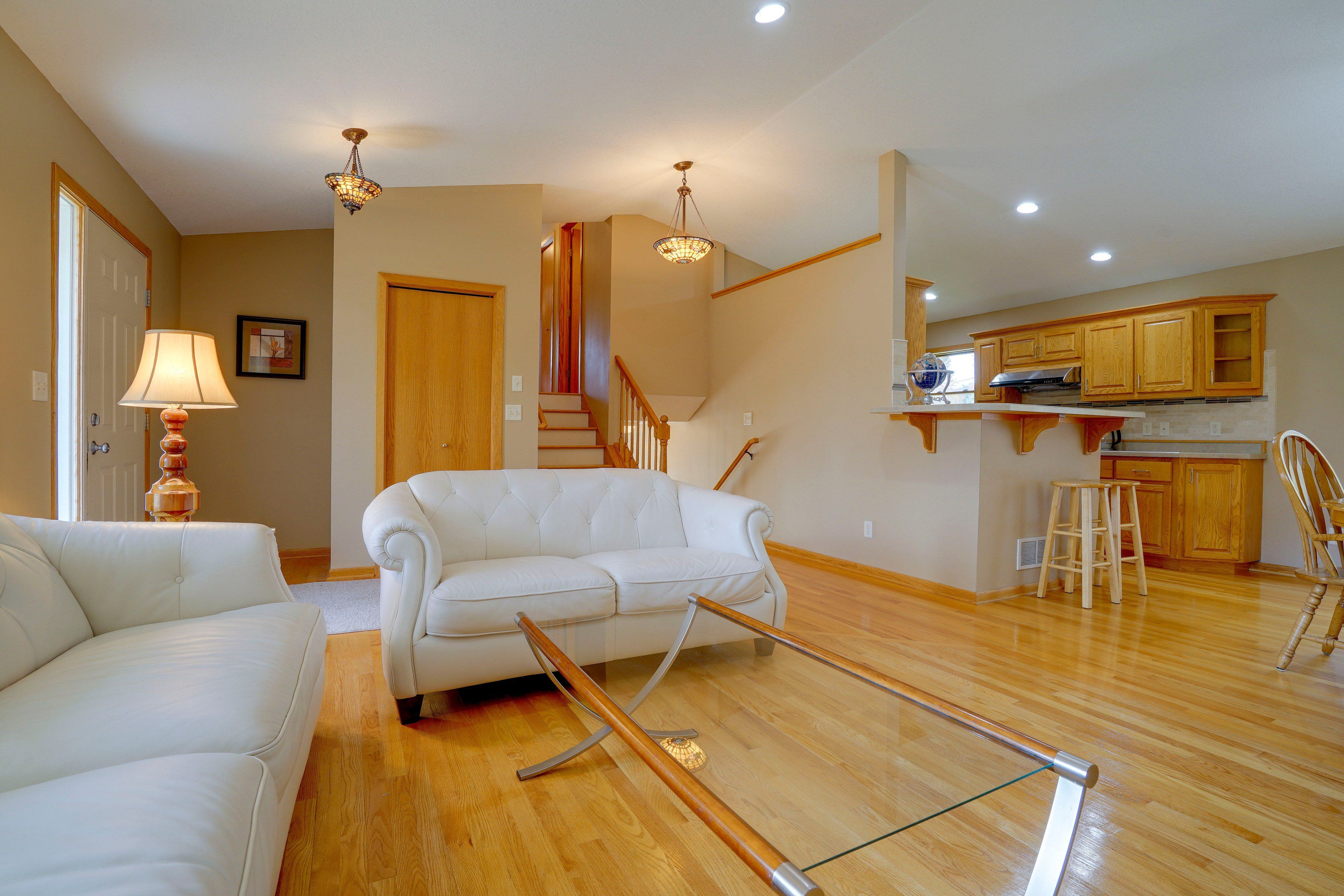 Un salon spacieux avec un canapé blanc, un escalier en bois et un coin cuisine.