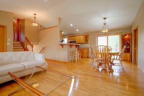 A spacious living area with a white sofa, wooden dining table, and chairs, a kitchen with wooden cabinets, and a staircase with wooden railings. - Northfield Home Near Nerstrand Big Woods (Northfield)