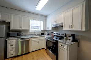 Una cocina moderna con armarios blancos, electrodomésticos de acero inoxidable y piso de madera.
