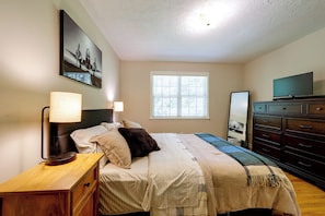 A bedroom with a bed, bedside lamp, dresser, television, and a window with blinds. - 6 Mi to the Masters: North Augusta Condo (North Augusta)