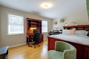 Un dormitorio con un escritorio de madera, una cama con muchos cojines, un sillón verde y un piano.