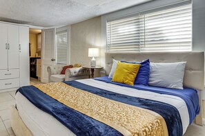 A bedroom with a bed, a wardrobe, a bedside table with a lamp, and a window with blinds. - Direct Daytona Beach Access & Views! Spacious Home (Daytona Beach Shores)
