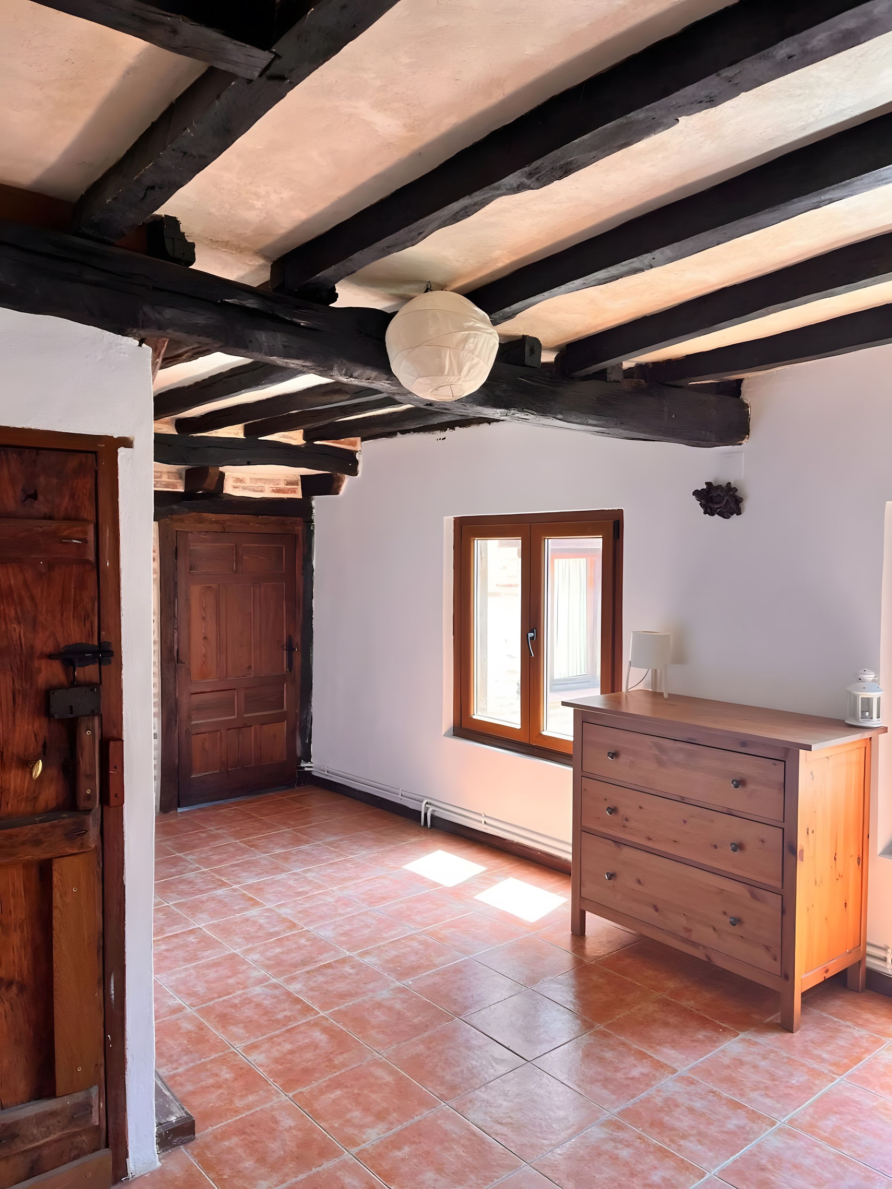 Une pièce avec un meuble en bois, une porte, une fenêtre et un sol carrelé.