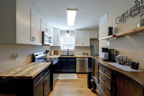 Una cocina con armarios blancos, encimera de madera, estación de café y lavavajillas.