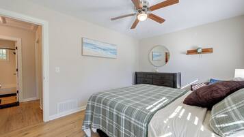 Un dormitorio con cama, ventilador de techo, cómoda, espejo y un cuadro en la pared.