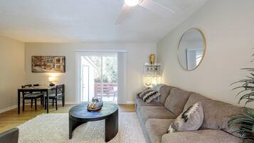 A living room with a sofa, a coffee table, a dining area with chairs, a painting, and a ceiling fan.